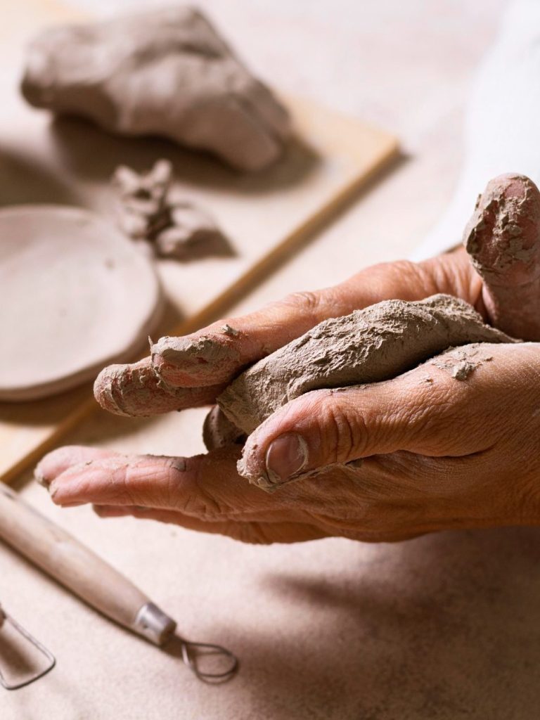 Keramik handgemacht in unserer Einrichtung Artikel aus Keramik. Hände formen Ton mit Werkzeugen und Schalen im Hintergrund.